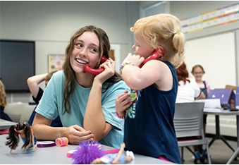A teacher and young student holding play phones to their ears.